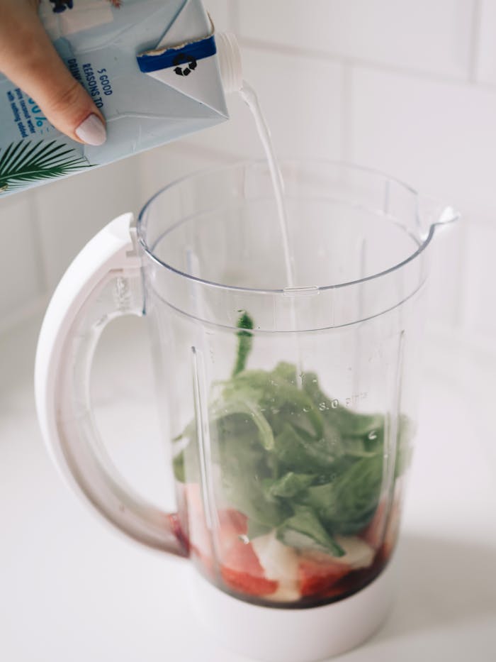 Pouring milk into blender with spinach, bananas, and strawberries for a fresh smoothie.