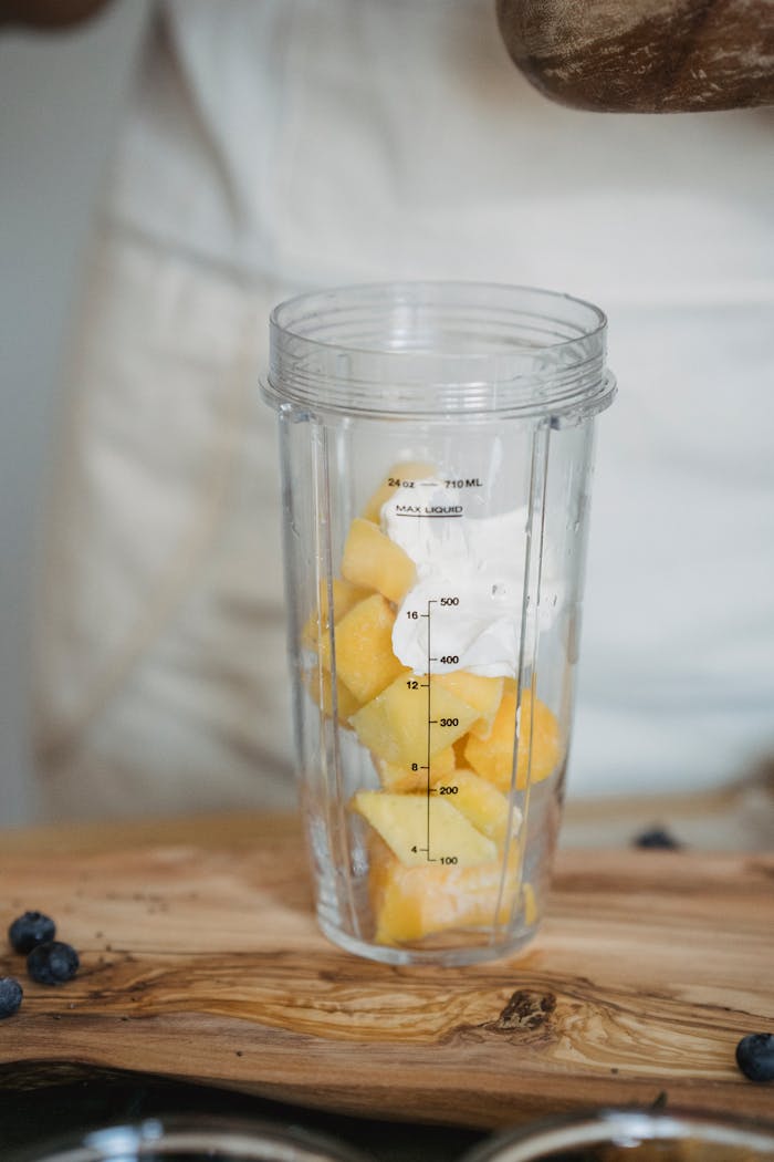 A close-up of mango chunks and yogurt in a blender cup on a wooden surface.