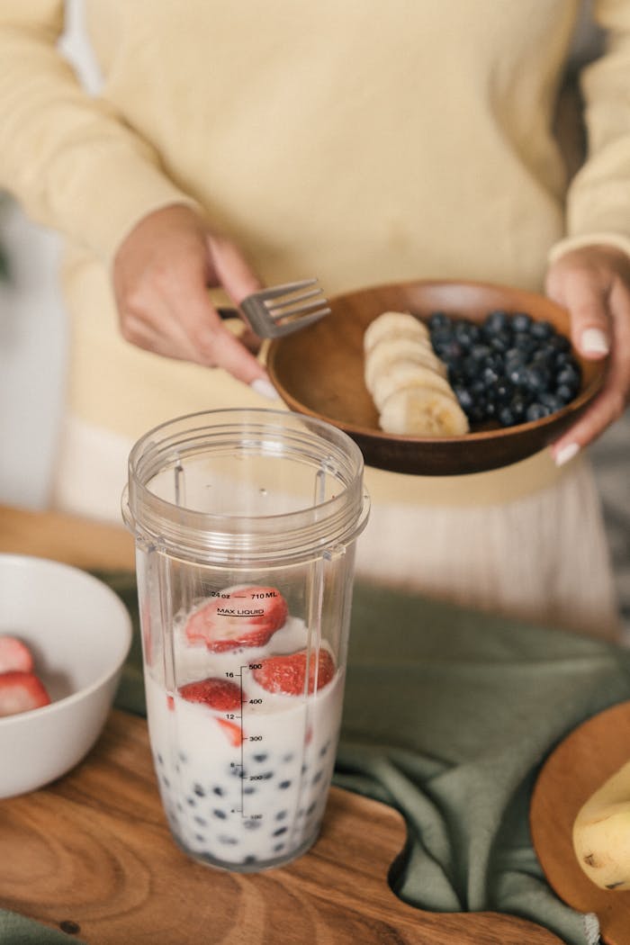 Person preparing a fruit smoothie with bananas, blueberries, and strawberries. Perfect for a healthy lifestyle.